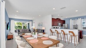 A modern living room with a dining area, kitchen, and a large window. - Spacious Pool Home Close To Disney (Kissimmee)