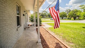Ein Backsteinhaus mit überdachter Veranda, einer amerikanischen Flagge und einem Rasen, im Hintergrund ein Auto.