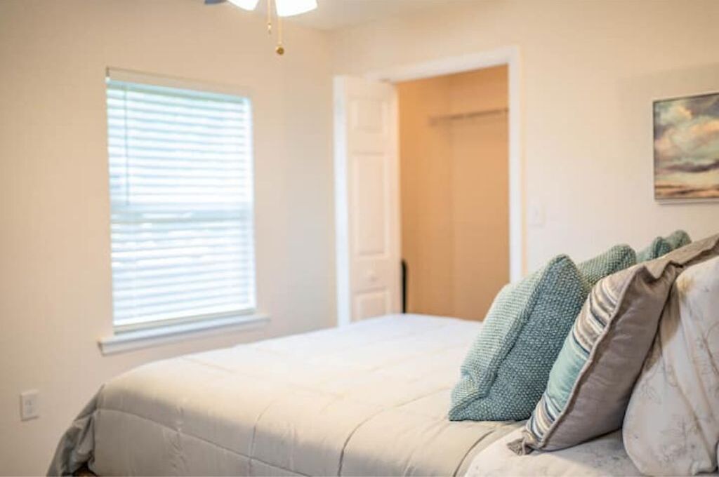 A bedroom with a bed, a window with blinds, a door, and a painting on the wall.