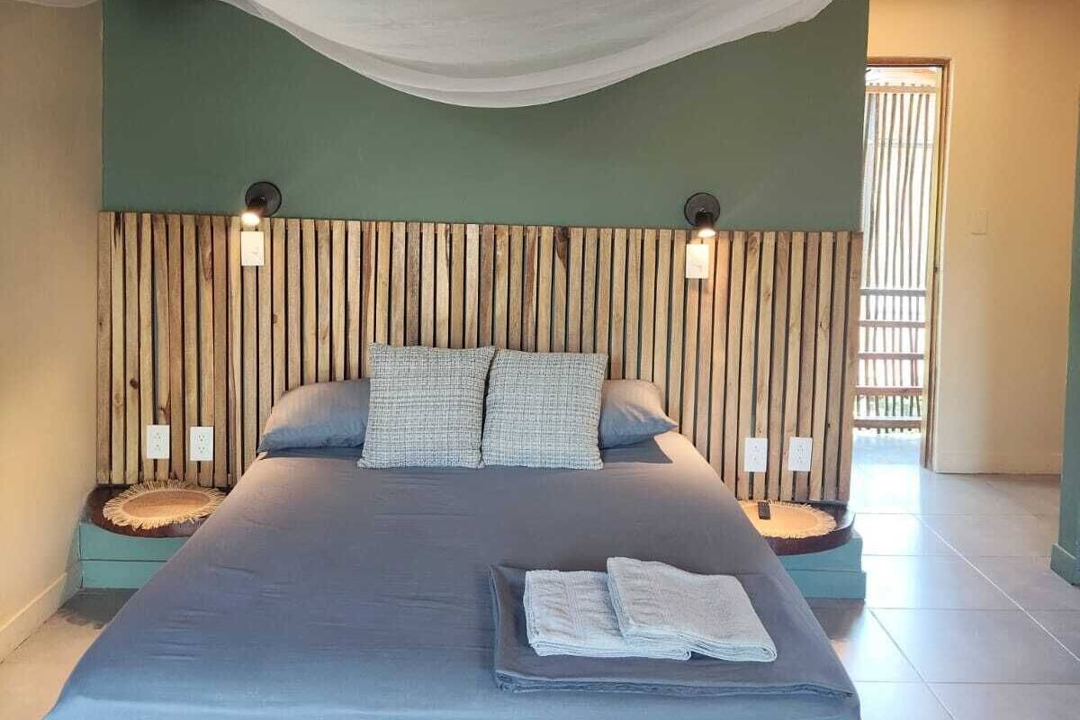 Un dormitorio con cama, dosel, cabecero de madera, lámparas de noche y vistas al exterior.
