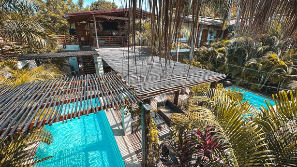 Área de piscina com deck de madeira e plantas tropicais.