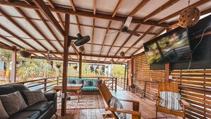 Um amplo deck de madeira com um sofá, cadeiras e uma TV fixada na parede.