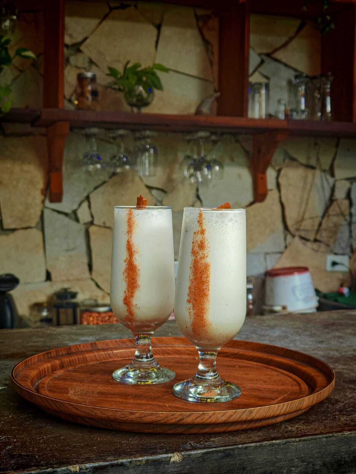 Two glasses of a white beverage with a brown garnish on a wooden tray.