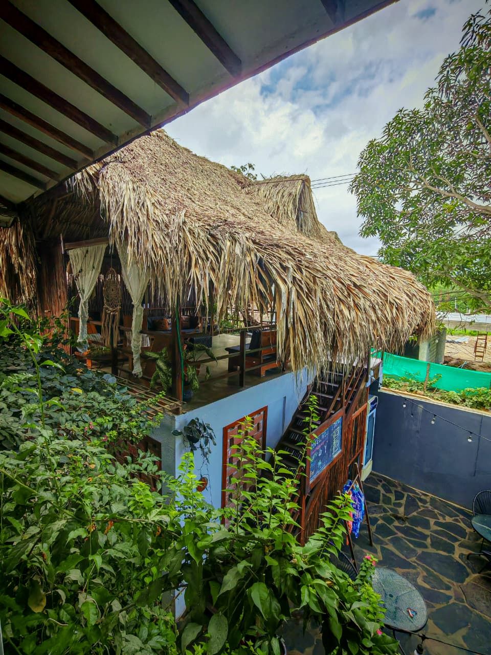 A thatched-roof structure with a balcony, surrounded by lush greenery.