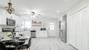 Une cuisine moderne avec des meubles blancs, une table à manger avec des chaises, un réfrigérateur et un ventilateur de plafond.