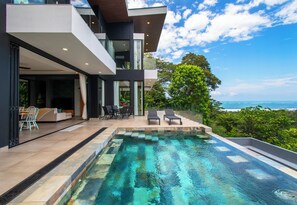 Et moderne hus med swimmingpool, udendørs siddepladser og udsigt til havet.