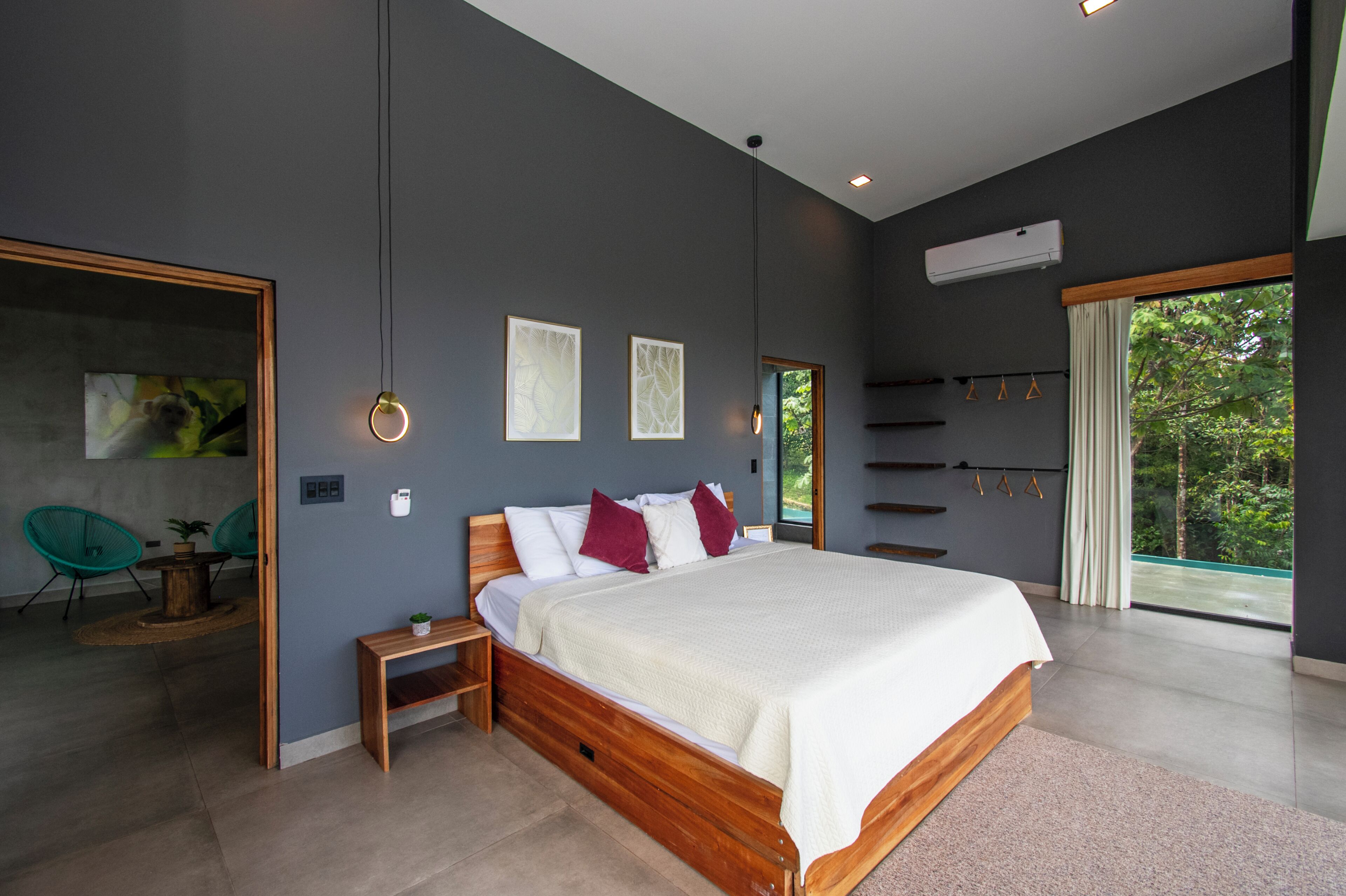 Un dormitorio moderno con una cama grande, una mesita de noche de madera, una pequeña mesa con una planta y vistas a zonas verdes a través de la ventana.