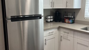 Une cuisine moderne avec des meubles blancs, un réfrigérateur en acier inoxydable, une machine à café et une bouilloire posées sur le plan de travail.