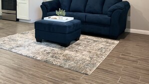 Un salon avec un canapé bleu foncé, un pouf assorti et un plateau blanc sur lequel sont posés une plante et un livre.