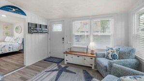 Une chambre de taille modeste comprenant un lit, un coin salon avec des coussins à motifs, un tapis décoré d’une étoile de mer et un téléviseur fixé au mur.