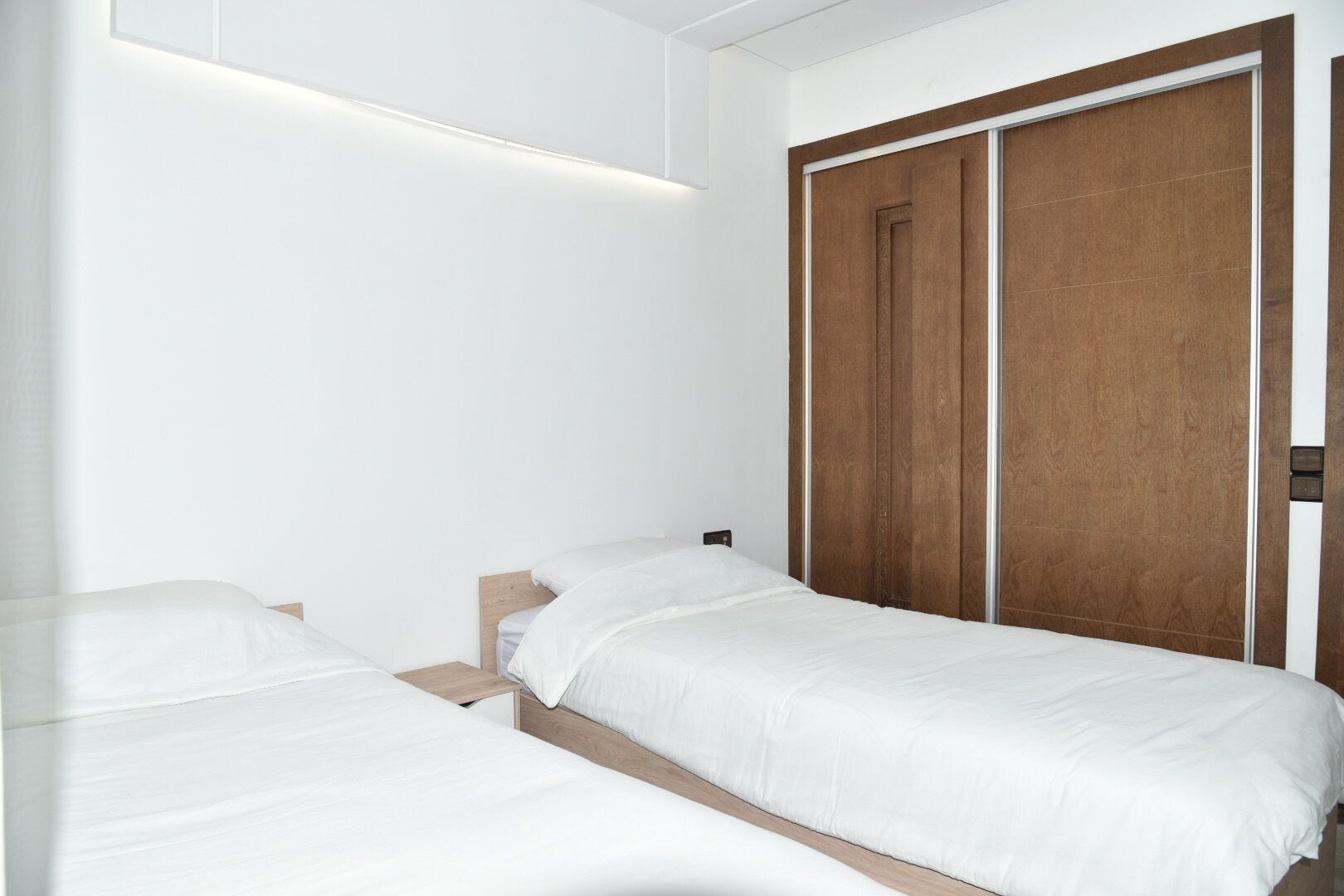 Een slaapkamer met twee eenpersoonsbedden, een houten garderobe en een moderne lamp.