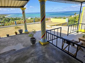 Un balcon offrant une vue sur l’océan, agrémenté de colonnes à rayures et de plantes en pot.