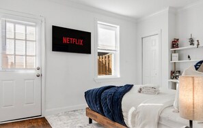 Une chambre à coucher avec un lit, un téléviseur fixé au mur, une fenêtre et une porte.