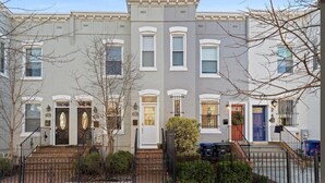 A row of three-story townhouses with a brick facade, white trim, and a central entrance with a black gate. - Entire Rowhome in Northwest Washington (Dedicated Parking Spot Available) (Washington)