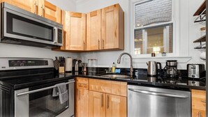 A modern kitchen with wooden cabinets, stainless steel appliances, and a window with a brick wall. - Entire Rowhome in Northwest Washington (Dedicated Parking Spot Available) (Washington)