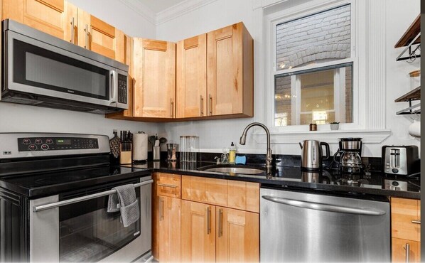 A modern kitchen with wooden cabinets, stainless steel appliances, and a window with a brick wall.