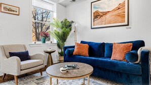 A living room with a blue sofa, a beige armchair, a round coffee table, and a large window with a view of trees. - Entire Rowhome in Northwest Washington (Dedicated Parking Spot Available) (Washington)