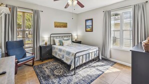 A bedroom with a bed, a chair, a desk, a ceiling fan, and a window with curtains. - Bonita Beach House by Ryson Vacation Rentals (Galveston)