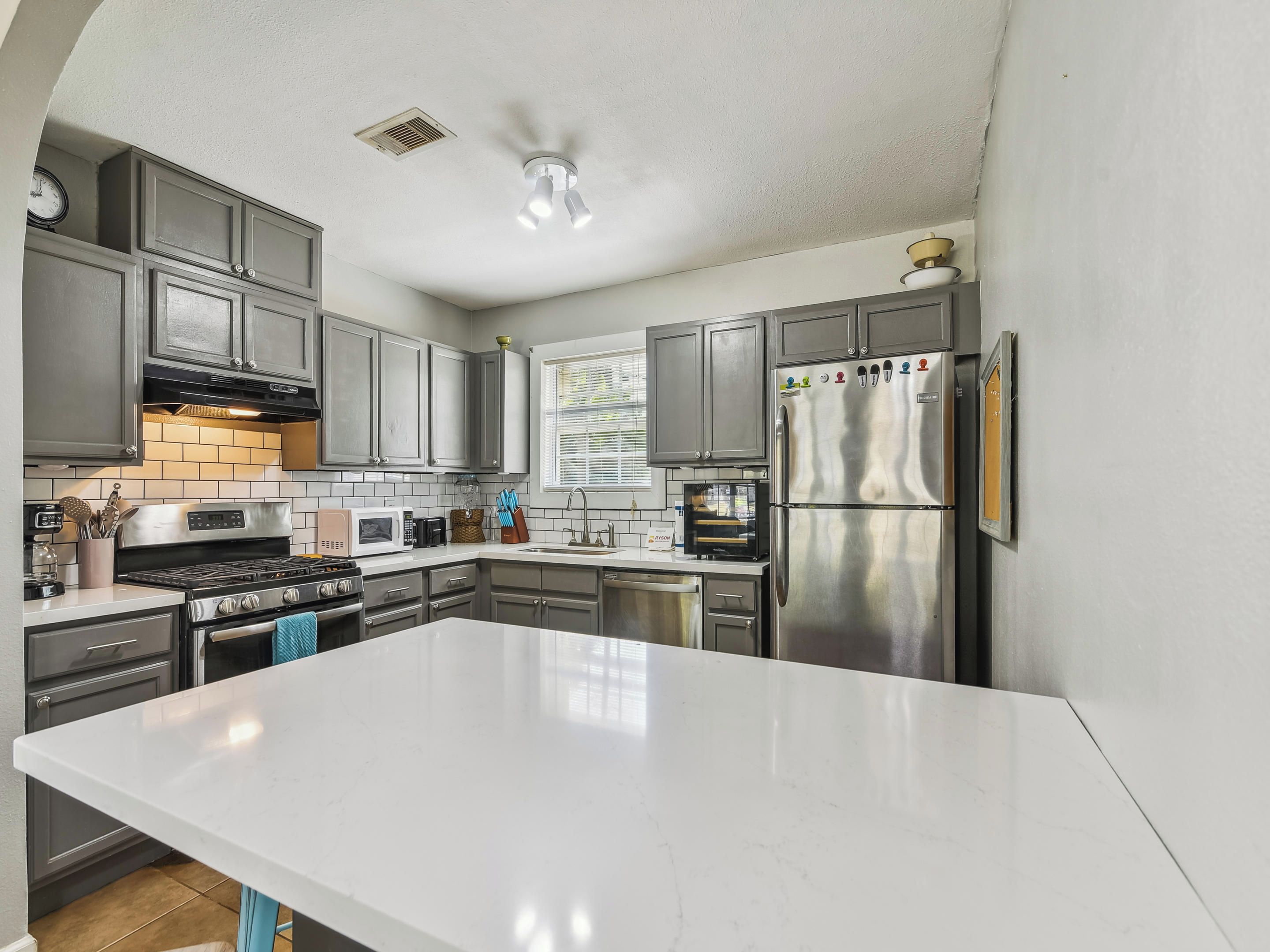 A modern kitchen with grey cabinets, a white countertop, stainless steel appliances, and a built-in oven.