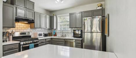 A modern kitchen with grey cabinets, a white countertop, stainless steel appliances, and a built-in oven.