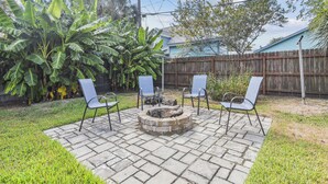 A backyard with a fire pit, three chairs, and a wooden fence. - Bonita Beach House by Ryson Vacation Rentals (Galveston)