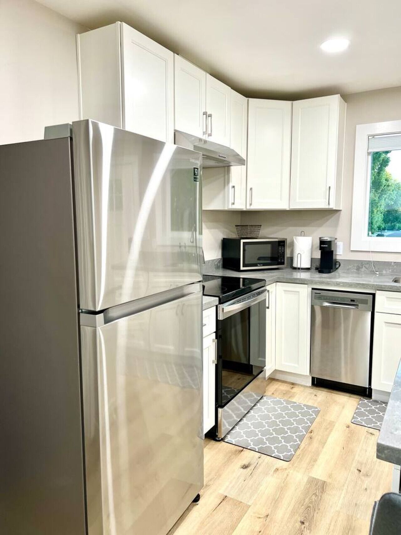 A modern kitchen with stainless steel appliances, white cabinets, and a window providing natural light.