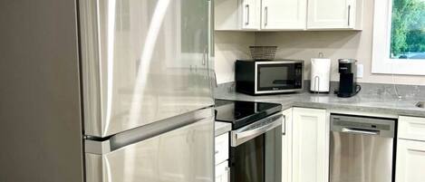 A modern kitchen with stainless steel appliances, white cabinets, and a window providing natural light.