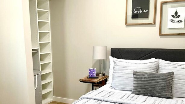 A bedroom with a bed, a nightstand, a lamp, a wardrobe, and two framed pictures on the wall.