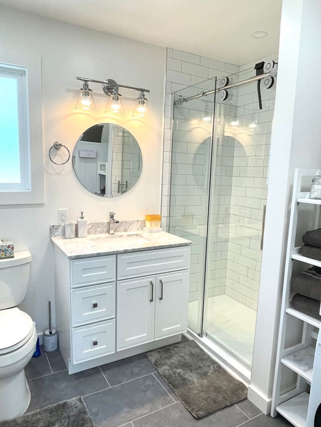 Une salle de bain moderne avec un meuble-lavabo blanc, un miroir rond et une cabine de douche en verre.