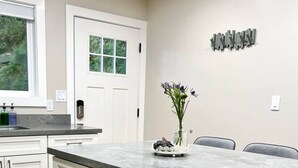 A modern kitchen with white cabinets, a marble countertop, and a dining area with grey chairs.