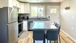 A modern kitchen with stainless steel appliances, a central island with seating, and a view of the outdoors through large windows.