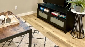 A modern living room with a flat-screen TV on a black stand, a wooden coffee table, and a small side table with a plant.