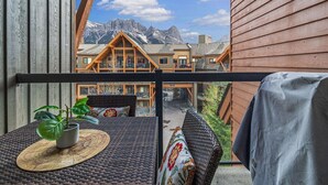 A balcony with wicker furniture, a potted plant, and a view of a mountain lodge.
