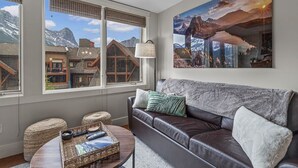 A living room with a leather sofa, a coffee table, and a large window with a mountain view.