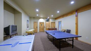 Una habitación con dos mesas de ping pong, una mesa de futbolín, un televisor y una puerta de madera.