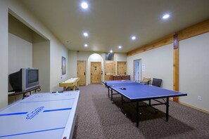A room with two ping pong tables, a foosball table, a television, and a wooden door.