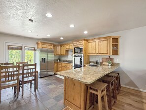 A kitchen with wooden cabinets, a stainless steel refrigerator, a granite countertop, and a bar stool seating area. - Eden Mountain Hideaway: King Suite-Hot Tub (Eden)