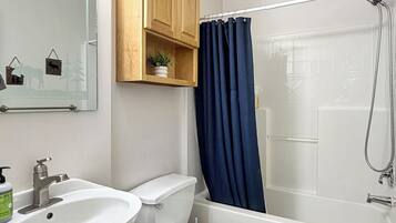 A bathroom with a sink, toilet, and bathtub. There is a mirror above the sink and a wooden cabinet above the toilet.