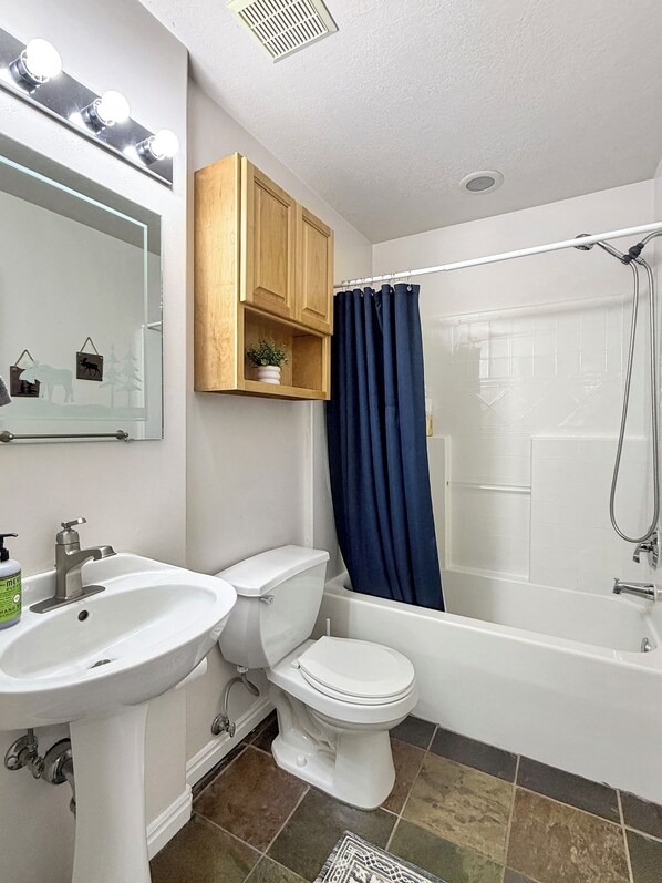 A bathroom with a sink, toilet, and bathtub. There is a mirror above the sink and a wooden cabinet above the toilet.