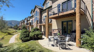 A residential building with multiple balconies, a patio area with outdoor furniture, and a view of a mountain range.