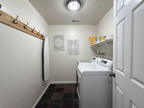 A laundry room with a washing machine, a drying rack, and a shelf with cleaning supplies.
