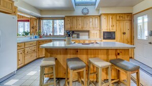 A kitchen with wooden cabinets, a large island with stools, a skylight, and a view of the outdoors. - 1-acre retreat with firepits, wraparound porch & a relaxing 6-person hot tub (Sisters)