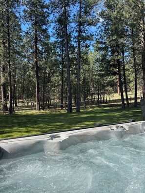 Un bain à remous entouré d’une zone boisée, avec de grands arbres et un champ d’herbe.