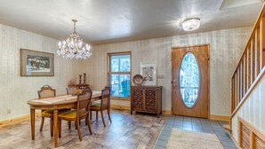 A dining room with a wooden table and chairs, a chandelier, and a view through a door to the outside. - 1-acre retreat with firepits, wraparound porch & a relaxing 6-person hot tub (Sisters)