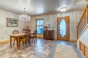 A dining room with a wooden table and chairs, a chandelier, and a view through a door to the outside.