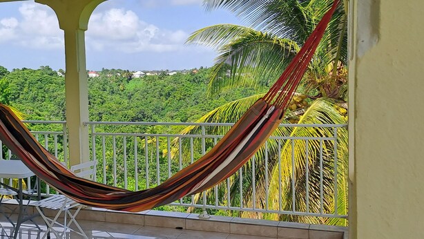 A hammock on a balcony with a view of lush greenery and houses in the distance. - Joss plein  air (Le Gosier)