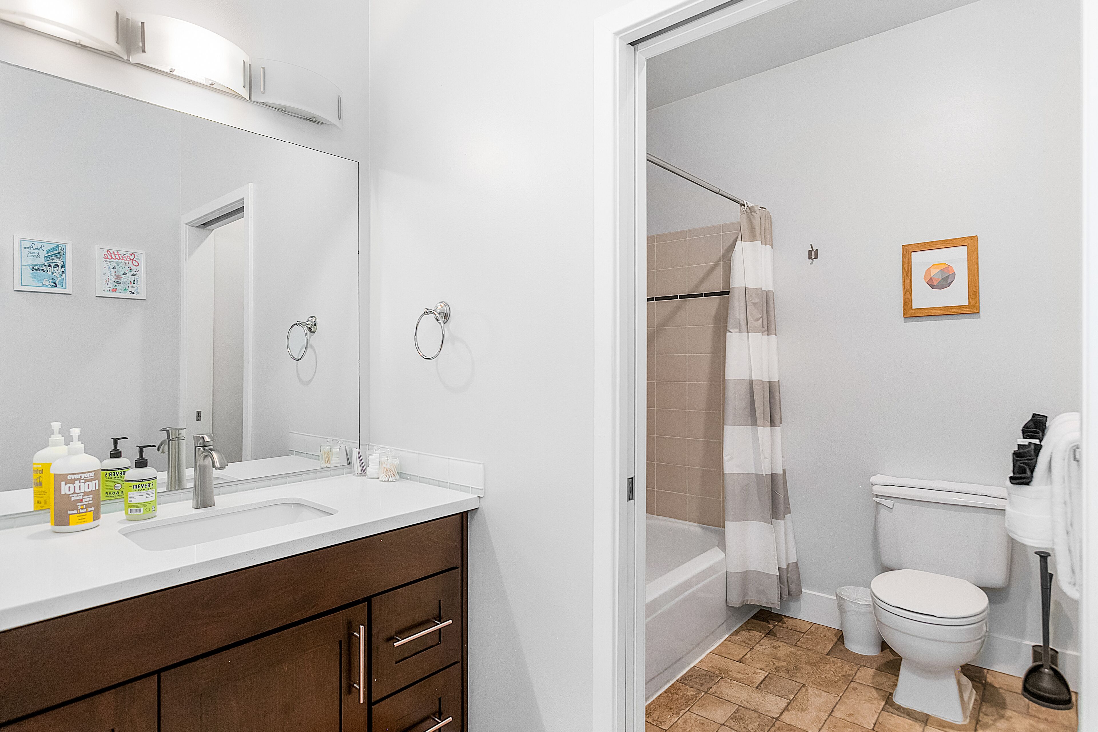 Une salle de bain avec un lavabo blanc, un miroir et des toilettes, une douche avec un rideau à rayures et un petit tableau encadré accroché au mur.