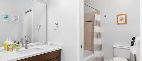 Une salle de bain avec un lavabo blanc, un miroir et des toilettes, une douche avec un rideau à rayures et un petit tableau encadré accroché au mur.