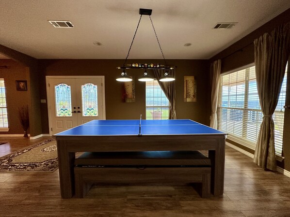 A room with a ping pong table, a chandelier, a door with stained glass, and large windows with curtains. - The Napoleon (Fort Stockton)