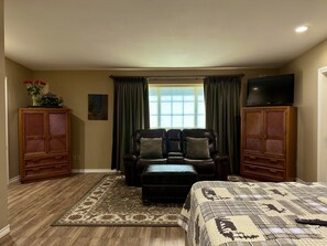 A room with a large bed, a leather sofa, a matching ottoman, and two wooden cabinets. A flat-screen TV is mounted on the wall above the sofa. - The Napoleon (Fort Stockton)